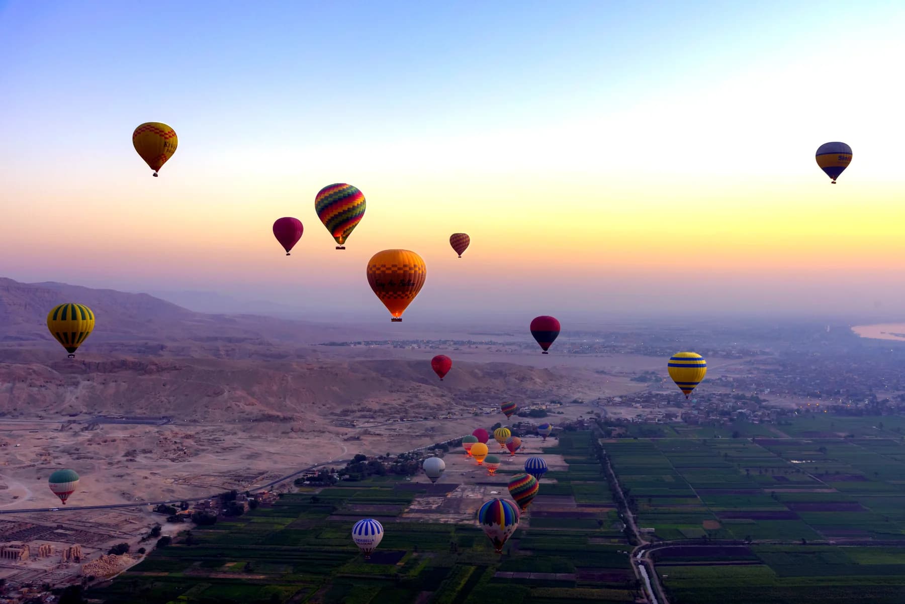 Colourful hot air balloons floating over the mountains and green fields of Luxor at sunrise